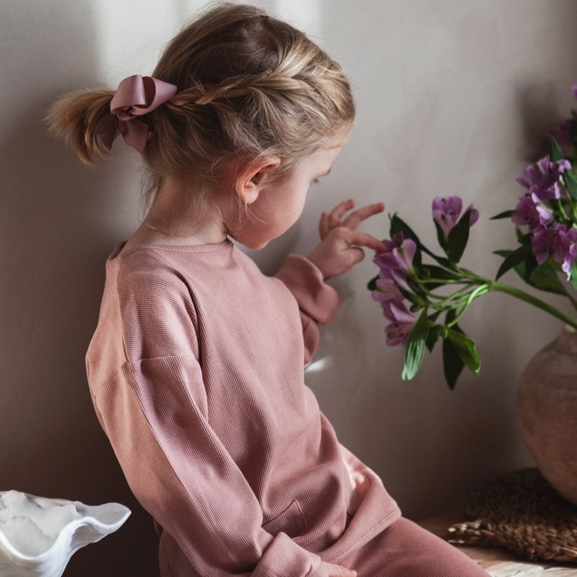 kleines Mädchen in Sweatshirt betrachtet eine Blüte